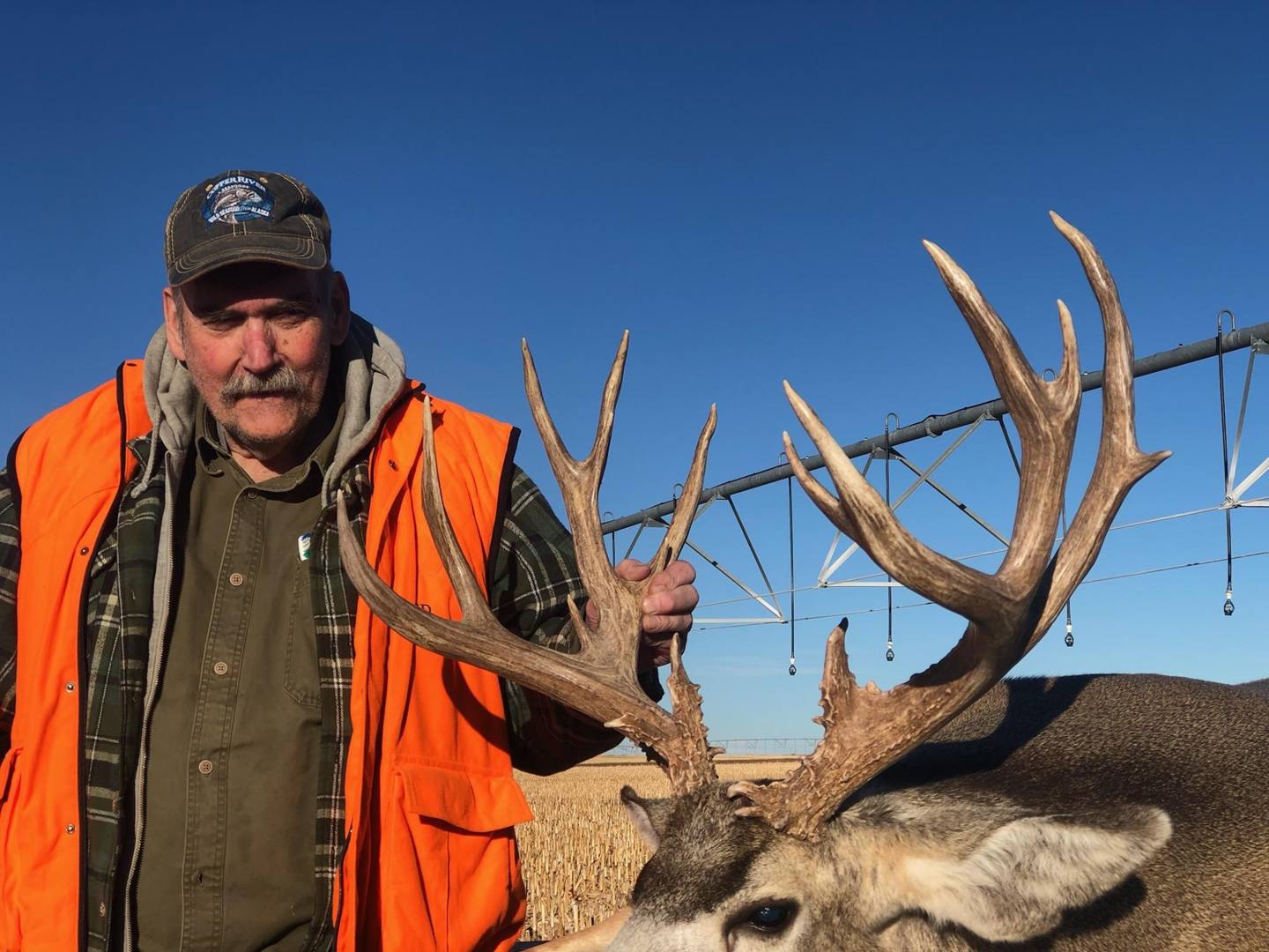 Hunter with a heavy typical mule deer buck under a Colorado blue sky