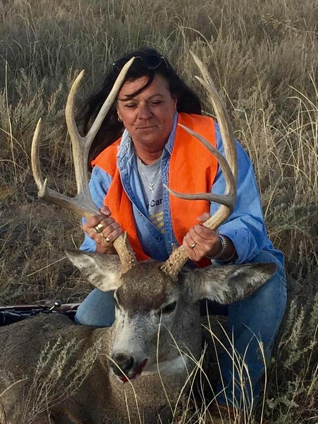 Hunter with a mule deer buck in the tall grass