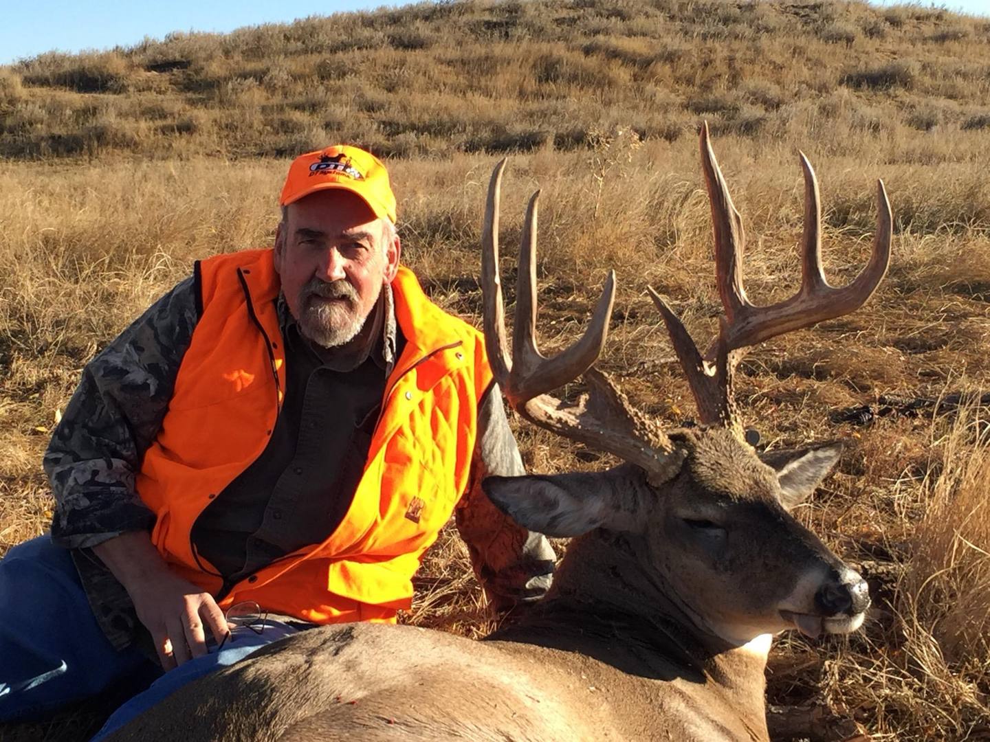 Hunter kneeling with a whitetail buck on a prairie hillside